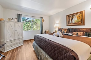Un dormitorio con una cama grande, un aparador, una ventana con cortinas, un cuadro en la pared y una lámpara en la mesita de noche.