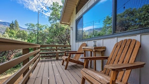 A wooden deck with chairs and a table, overlooking a forested area. - Cedar Pine Cottage | Relaxing Cozy 2BR Cabin (Springville)