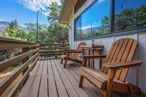 Une terrasse en bois, avec des chaises et une table, donnant sur une zone boisée.