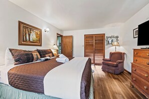 Habitación de hotel con una cama grande, una silla, un tocador, un televisor y un cuadro en la pared.
