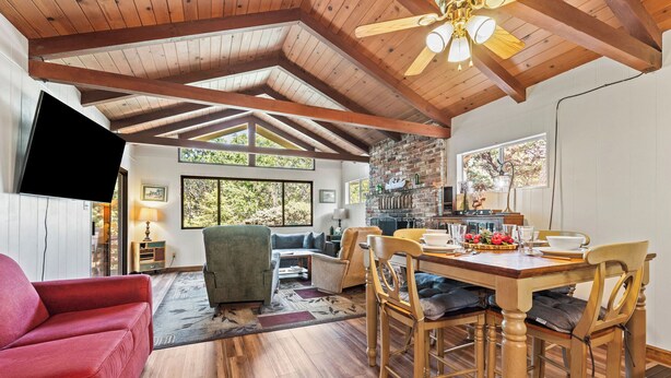A spacious living area with a dining table, wooden ceiling beams, and a fireplace. - Cedar Pine Cottage | Relaxing Cozy 2BR Cabin (Springville)