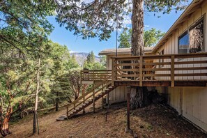 Un escalier en bois mène à un chalet d’où l’on peut admirer une forêt et des montagnes en arrière-plan.