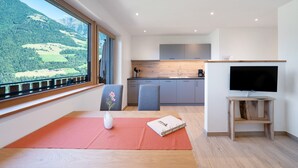 A modern room with a large window, a wooden table, a vase with flowers, a book, and a television on a stand. - Farmhouse 'Mutspitze' with Mountain View, Shared Garden and Wi-Fi (Scena)