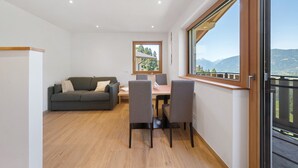 A modern living room with a sofa, dining table, chairs, and a large window with a mountain view. - Farmhouse 'Mutspitze' with Mountain View, Shared Garden and Wi-Fi (Scena)