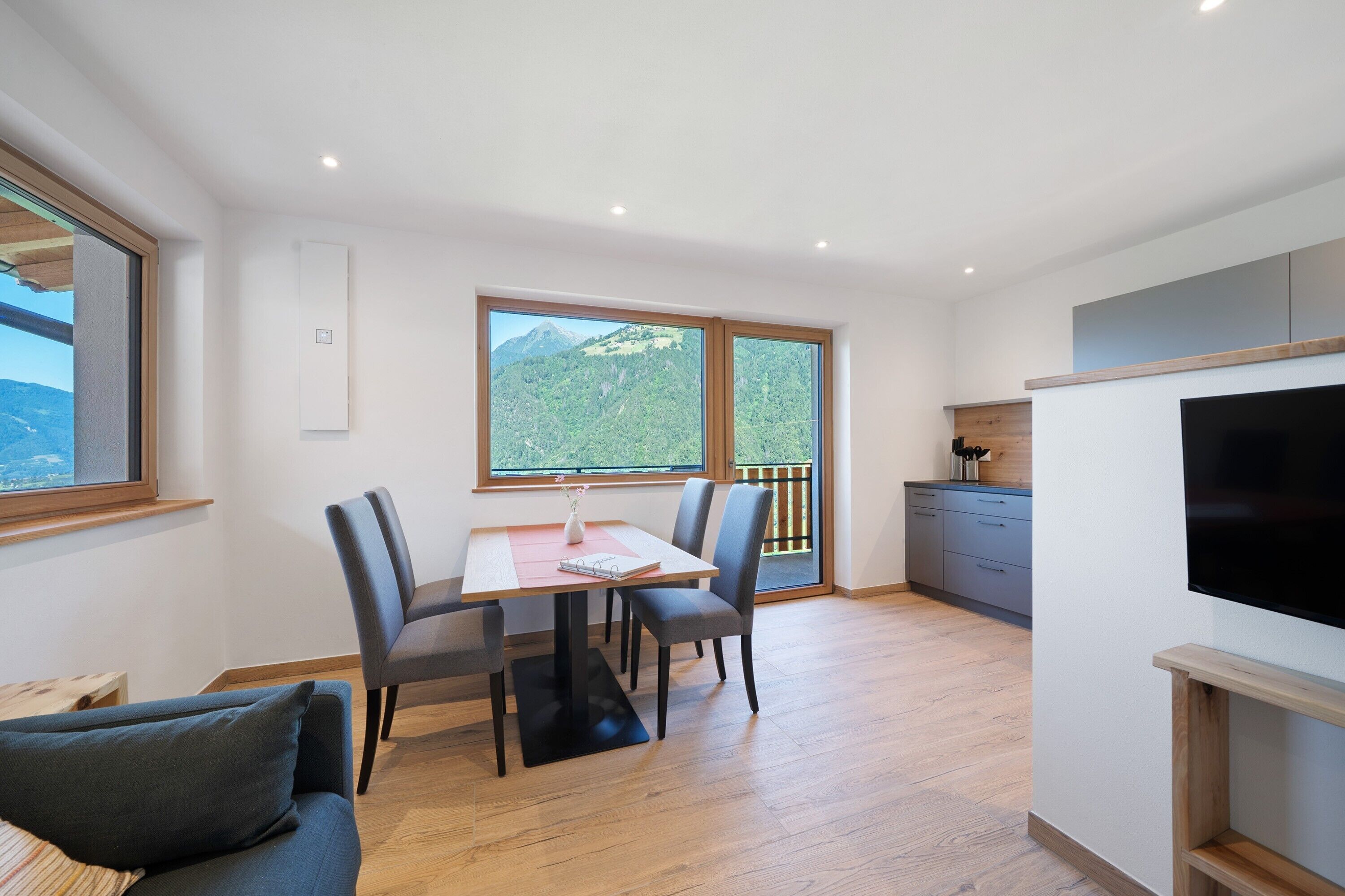 Une cuisine moderne équipée d’un téléviseur, dotée d’un plancher en bois et comprenant un coin repas avec une table et des chaises.