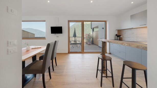 A modern kitchen with a wooden countertop, a dining area with a table and chairs, and a sliding glass door leading to an outdoor patio.