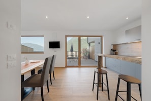 Une cuisine moderne avec un plan de travail en bois, un coin repas avec une table et des chaises, et une porte-fenêtre coulissante donnant sur une terrasse extérieure.