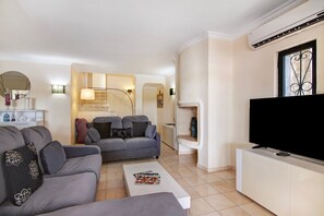 A modern living room with a sofa, coffee table, TV, and a staircase leading to another level. - Apartment 'Tennis View' with Private Pool, Wi-Fi and Air Conditioning (Almancil)