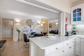 A modern kitchen with white cabinetry, a marble countertop, and a dining area with a table and chairs. - Apartment 'Tennis View' with Private Pool, Wi-Fi and Air Conditioning (Almancil)
