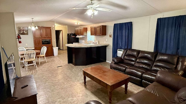A living room with a brown leather sofa, a wooden coffee table, and a dining area with white chairs. - Venice fishing/hunting lodging (Boothville-venice)