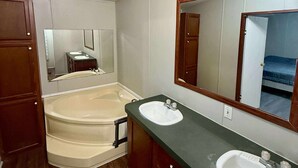 A bathroom with a bathtub, two sinks, wooden cabinets, and a mirror. - Venice fishing/hunting lodging (Boothville-venice)