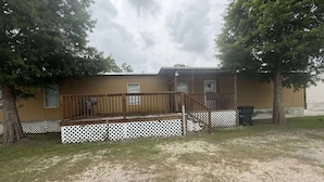 A single-story mobile home with a wooden deck and a fenced yard. - Venice fishing/hunting lodging (Boothville-venice)