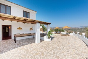 Une terrasse dallée de pierres, dotée d’un espace salon extérieur, d’une pergola et offrant une vue sur la campagne.
