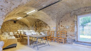 A rustic stone room with a bed, a table, and several chairs. - Holiday Home 'Mas Des Genêts' with Mountain View, Balcony and Wi-Fi (Laurac-en-Vivarais)
