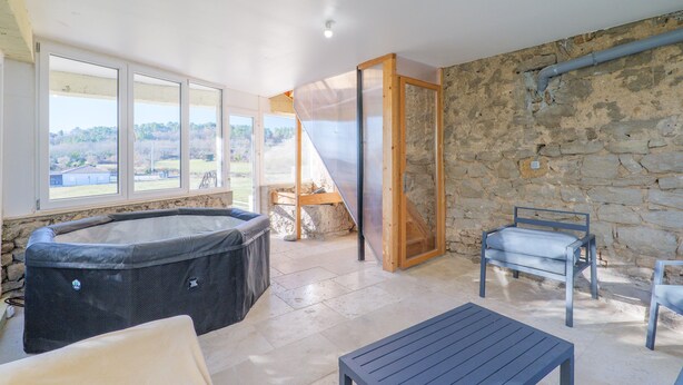 A room with a hot tub, a table, and chairs, with a stone wall and a view of the outdoors. - Holiday Home 'Très Belle Maison' with Mountain View, Balcony and Wi-Fi (Laurac-en-Vivarais)