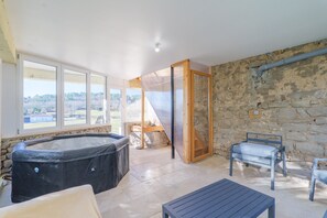A room with a hot tub, a table, and chairs, with a stone wall and a view of the outdoors. - Holiday Home 'Très Belle Maison' with Mountain View, Balcony and Wi-Fi (Laurac-en-Vivarais)