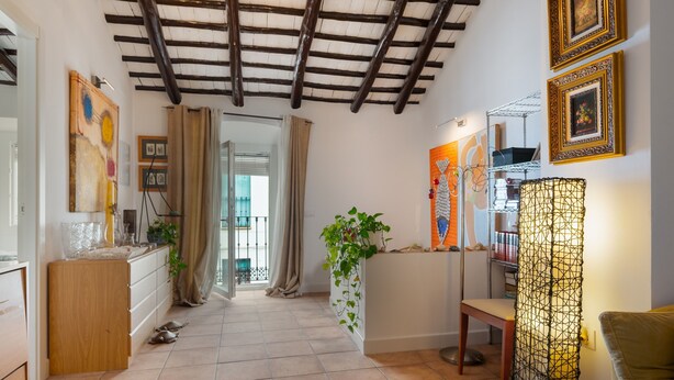 Un couloir avec un plafond en bois, une plante, une lampe et des œuvres d’art accrochées aux murs.
