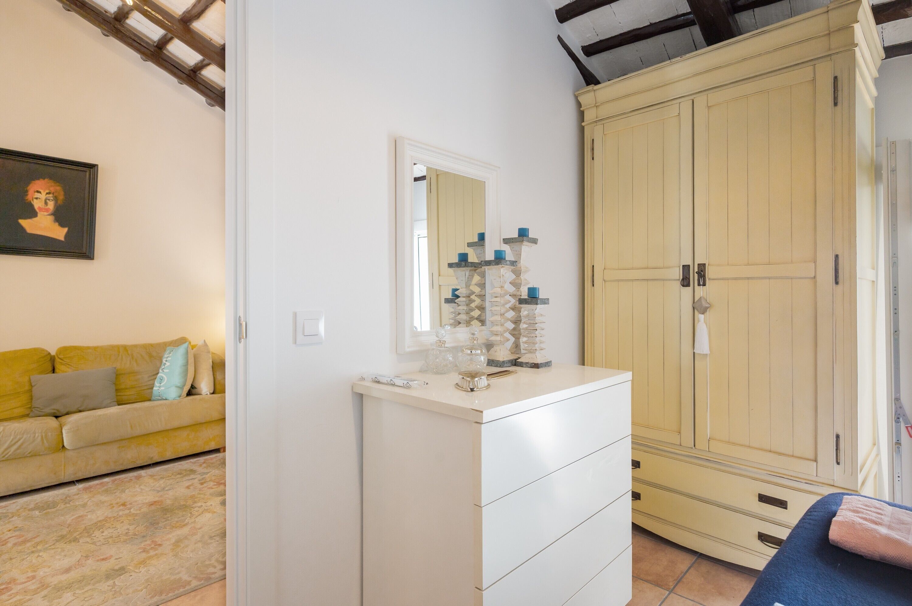Een kamer met een witte dressoir, een gele bank, een grote kast en een spiegel.