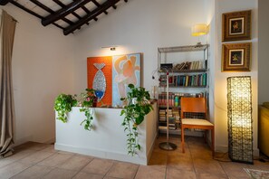 A reception desk with plants, a bookshelf, a chair, and framed pictures on the wall.