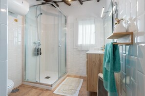 A modern bathroom with a glass-enclosed shower, white tiled walls, a wooden vanity, and a teal towel.
