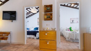 Une chambre avec une télévision, une commode en bois et un lit recouvert d’une courtepointe blanche.