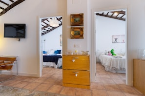 Une chambre avec une télévision, une commode en bois et un lit recouvert d’une courtepointe blanche.