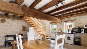 A kitchen with wooden beams, a washing machine, and a dining area with a table and chairs.