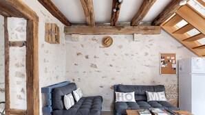 A rustic room with wooden beams, two blue sofas with cushions, a wooden table with magazines, and a bulletin board on the wall.