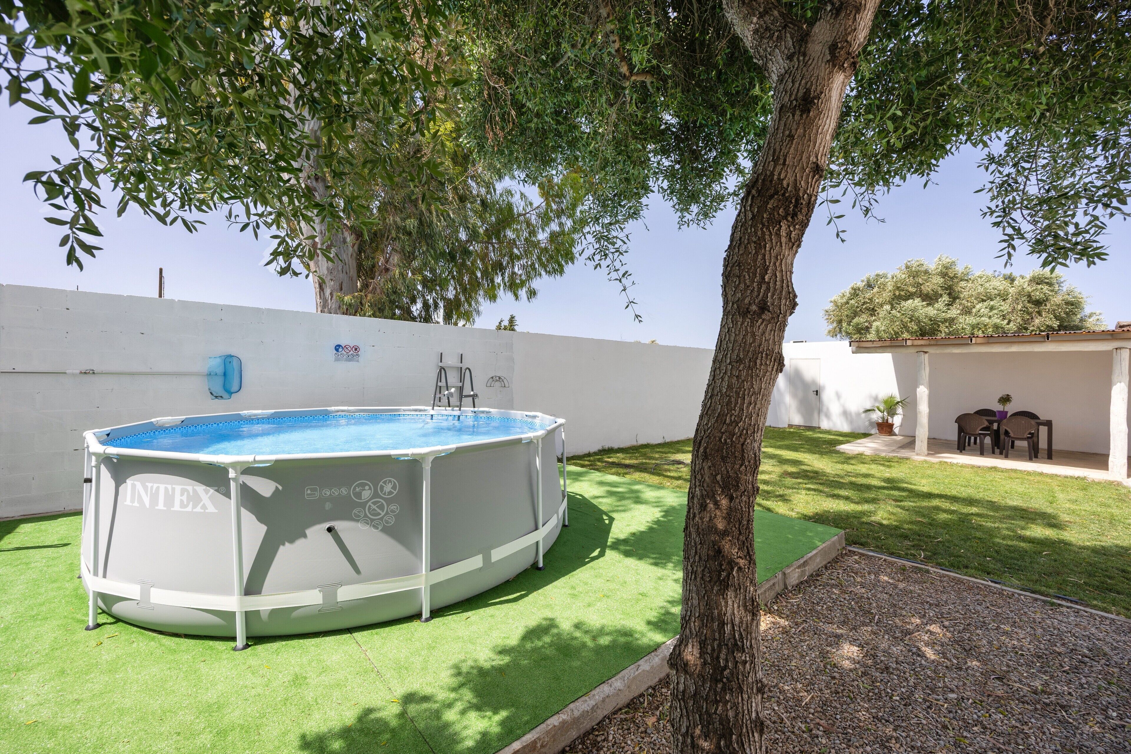 An outdoor swimming pool with a ladder, surrounded by artificial grass and a tree.