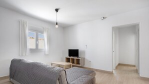 A modern living room with a sofa, a TV on a wooden stand, and a window with curtains.