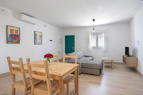 Una habitación con una mesa de comedor, sillas, un sofá, un televisor y un armario.