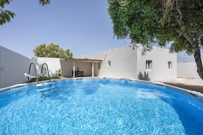 Une piscine à l’eau d’un bleu cristallin, entourée d’un bâtiment blanc doté d’un toit plat et d’un arbre situé sur la droite.