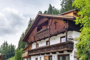 A traditional wooden chalet with a balcony, a wooden staircase, and a mountain backdrop.