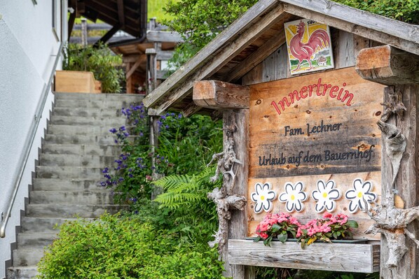 A wooden sign with 'Innkrein' and 'Fam. Lechner' written on it, a wooden staircase, and a flower box with pink flowers.