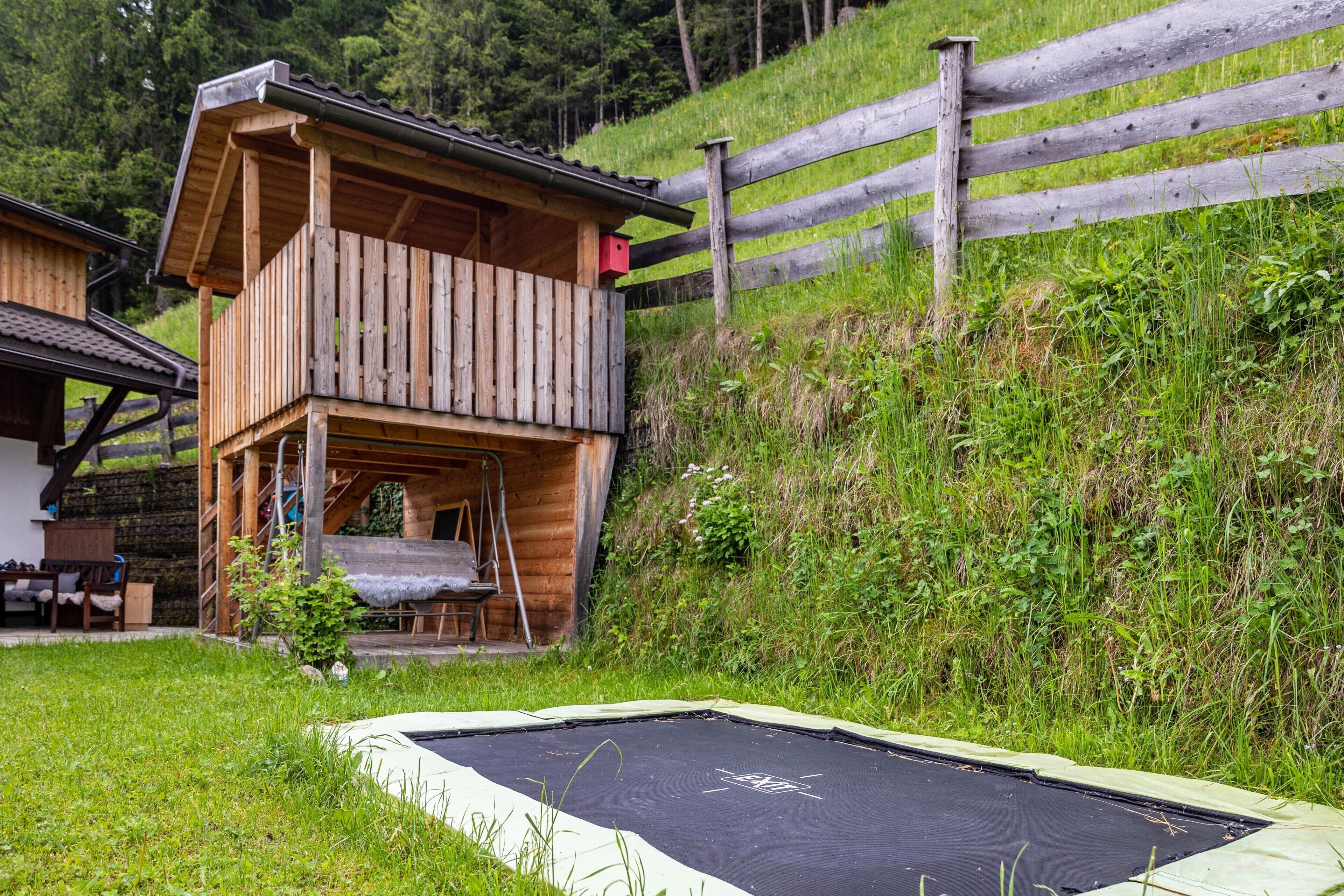 Una casetta in legno con un balcone, un trampolino e una recinzione in legno.