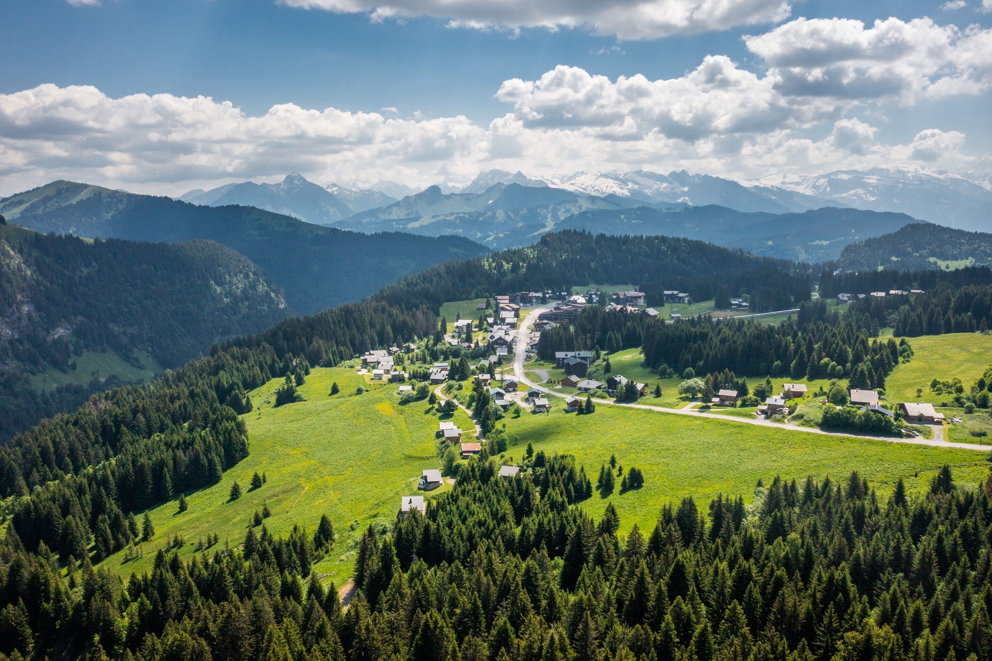 A village with houses and a road, surrounded by mountains and forests.