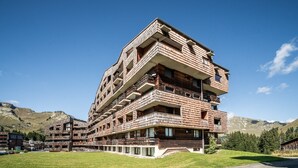 Een hotel met meerdere verdiepingen, balkons, een grindpad en een bergachtige achtergrond.