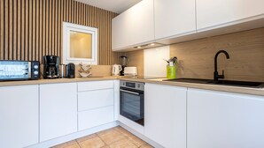 Una cocina moderna con armarios blancos, un zócalo de madera, horno empotrado y pileta.
