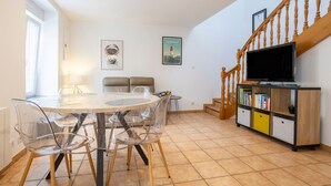 Un comedor con una mesa redonda y sillas, una escalera con barandillas de madera, y un televisor sobre un mueble de madera.