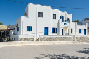 A white building with blue doors and windows, stone walls, and a clear blue sky.