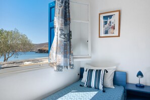Un dormitorio con cama, mesita de noche, lámpara, ventana con cortinas e imagen enmarcada en la pared.