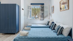 A bedroom with two beds, a wardrobe, a window with a view, and a painting on the wall. - Apartment 'Salonikia Studio No 3' with Sea View, Wi-Fi and Air Conditioning (Astypalaia)