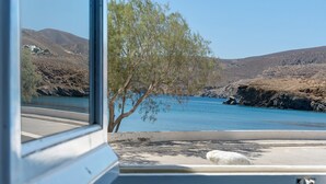 A view through a window of a coastal landscape with a tree, a body of water, and hills. - Apartment 'Salonikia Studio No 3' with Sea View, Wi-Fi and Air Conditioning (Astypalaia)