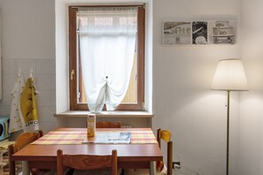 A room with a wooden table, chairs, a window with curtains, a lamp, and wall decorations.