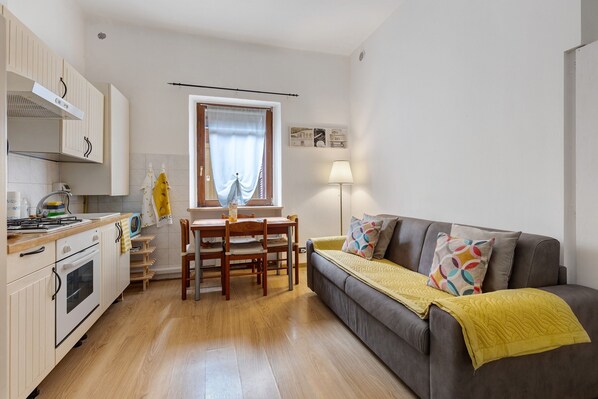 A compact living space with a kitchenette, dining area, and a sofa with a yellow throw.