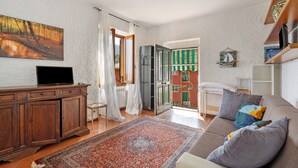 Una sala de estar con un sofá, un televisor sobre un mueble de madera, un tapete estampado y un cuadro de un paisaje boscoso.
