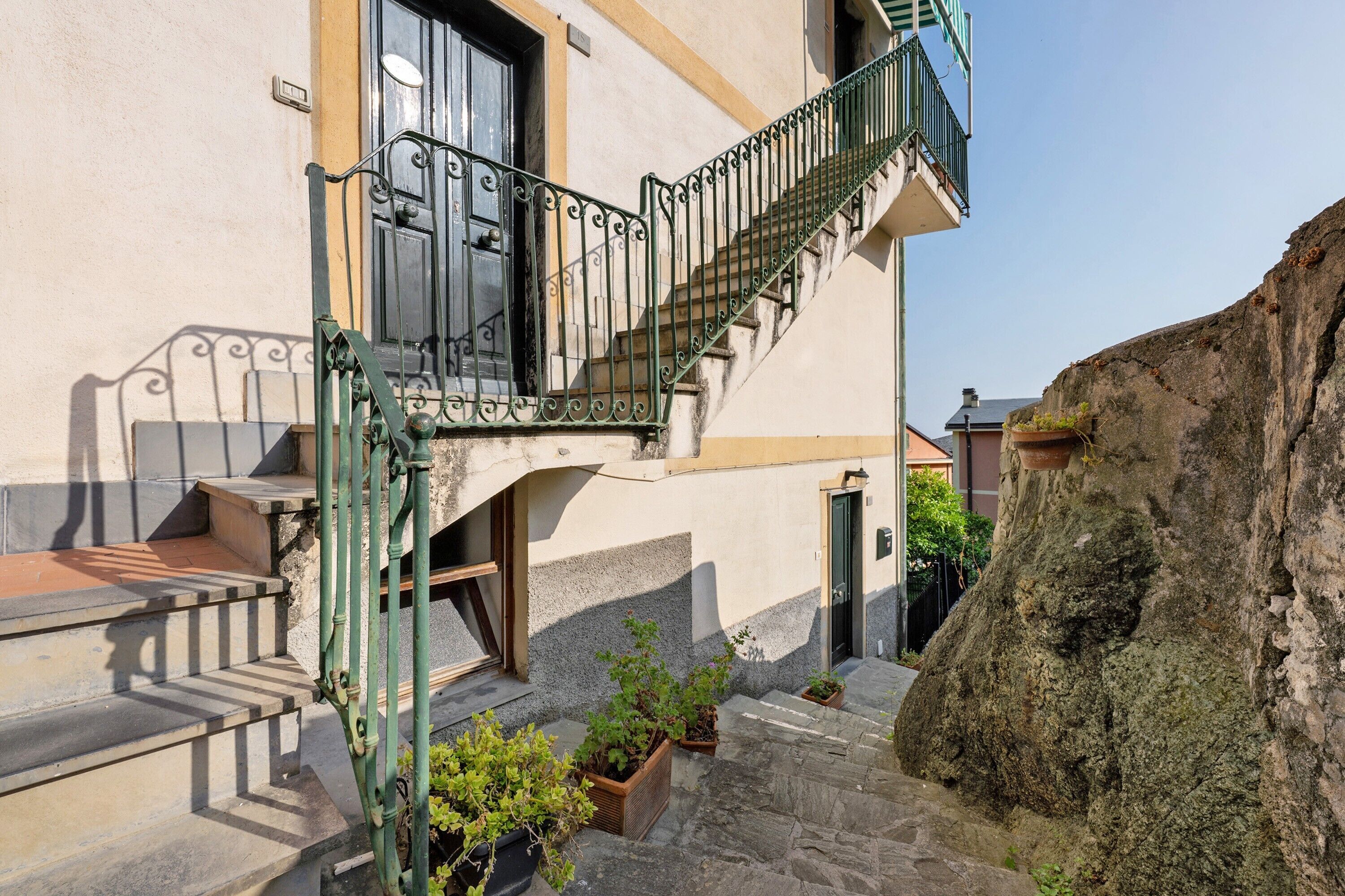 Ein Gebäude mit einer Treppe zu einem Balkon, einer Steinmauer und Kübelpflanzen.