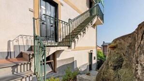 Un edificio con una escalera que lleva a un balcón, una pared de piedra y plantas en macetas.