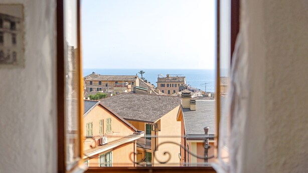 Vista desde una ventana sobre un pueblo costero con edificios y el mar al fondo.