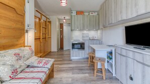 A compact living space with a kitchenette, a sofa with floral bedding, and a television. - Well-Equipped Studio with Enclosed Balcony and Mountain View (La Morte)